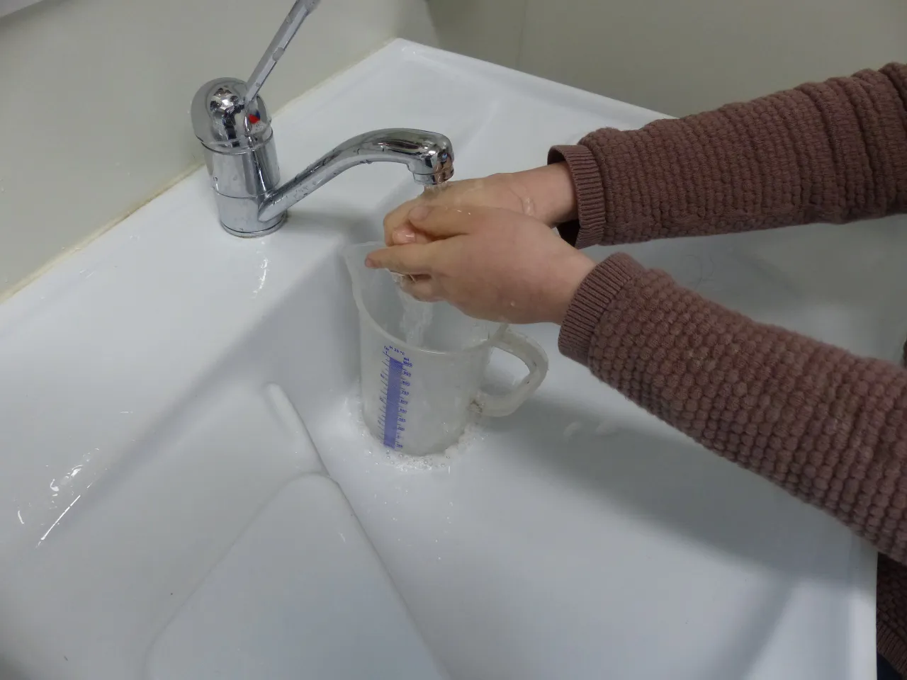 H&auml;ndewaschen &uuml;ber Messbecher am Waschbecken