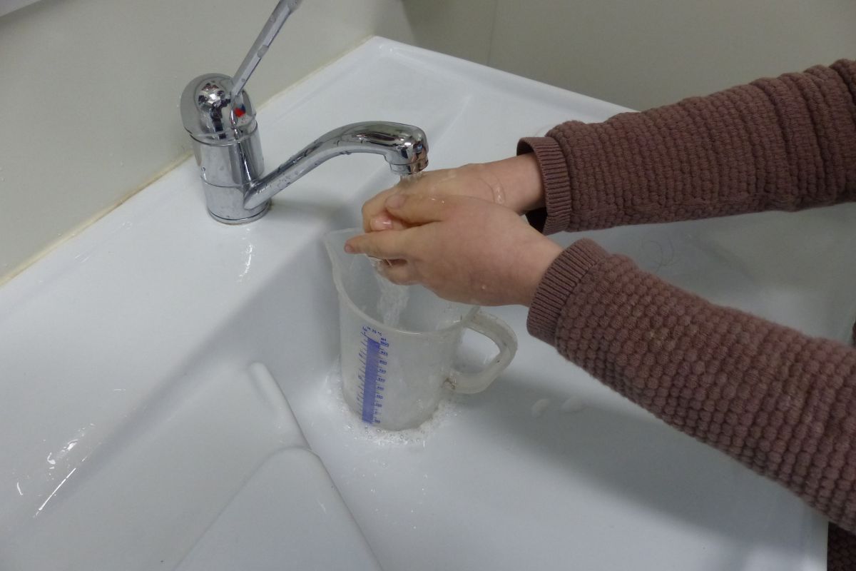 Händewaschen über Messbecher am Waschbecken
